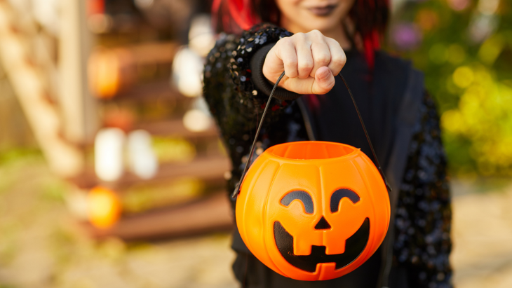 child wearing a costume and holding a jack-o-lantern bucket trick-or-treating on Halloween