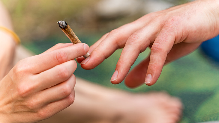 Close up of a person's hand holding a legal marijuana joint passing it to another person's hand