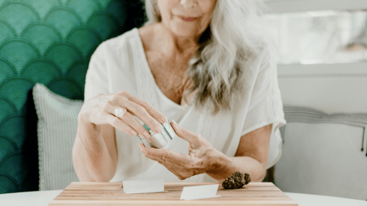 A senior woman uses a grinder to prepare cannabis for rolling into a joint
