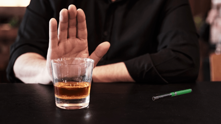 A person sitting at a bar holds up their hand saying "no" to an alcoholic beverage representing choosing cannabis over alcohol