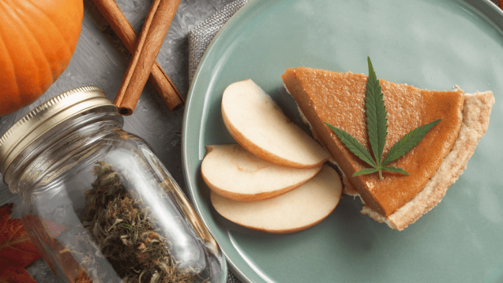 a slice of pumpkin pie topped with a small cannabis leaf is served with three apple slices on a ceramic plate