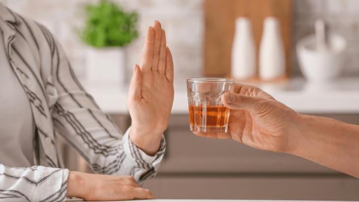 a woman raises her hand to signal no to the person offering a glass of liquor