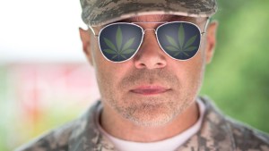 A veteran wears a camouflage hat and shirt and sunglasses with cannabis leaves reflecting on the lenses