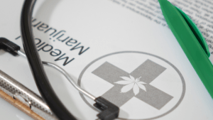 A stethoscope is draped across a clipboard holding a medical marijuana certification form and a green pen