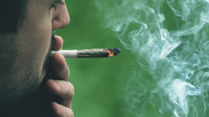 a man holds a cannabis joint to his lips and inhales