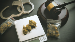 Handcuffs and a gavel sit on a table next to a small kitchen scale and two small bags of marijuana