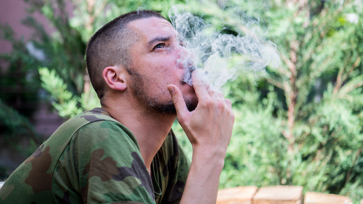 A man in a camouflage t-shirt smokes a legal cannabis joint, representing veteran marijuana use