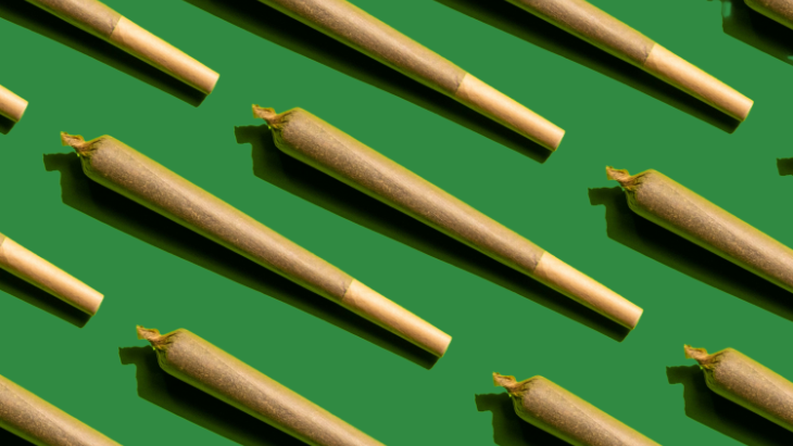 A uniform pattern of preroll marijuana joints on a green background