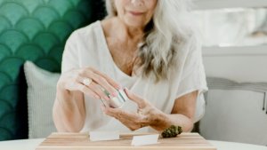 A senior woman uses a grinder to prepare cannabis for rolling into a joint
