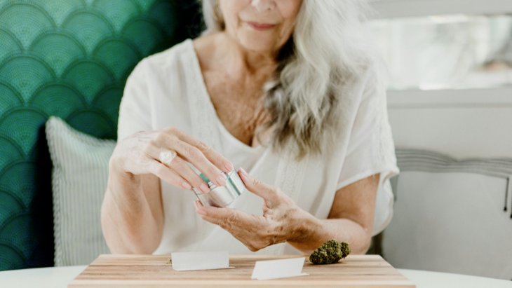 A senior woman uses a grinder to prepare cannabis for rolling into a joint